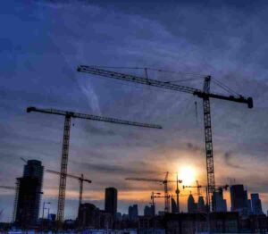 Idle construction cranes silhouetted against the Toronto skyline at sunset.